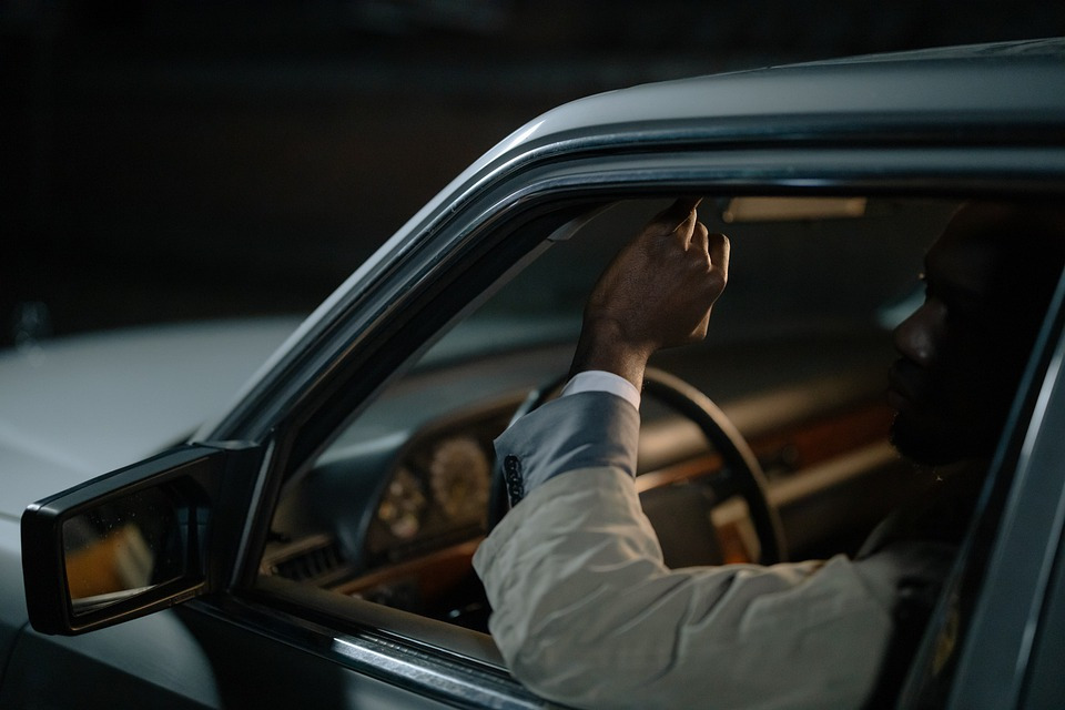 a man wearing a coat, sitting inside his dimly lit car
